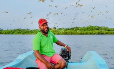 Smiling boat operator with herons flying above the Madu River wetlands