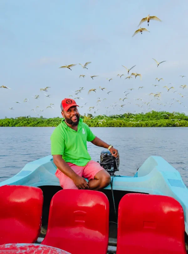 Smiling boat operator with herons flying above the Madu River wetlands